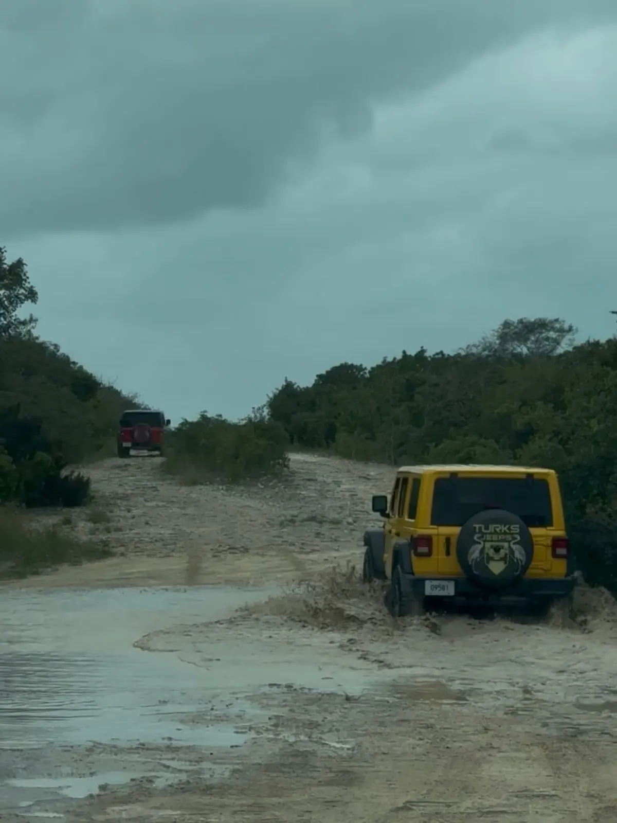 A yellow Wrangler following a red one down a dirt track
