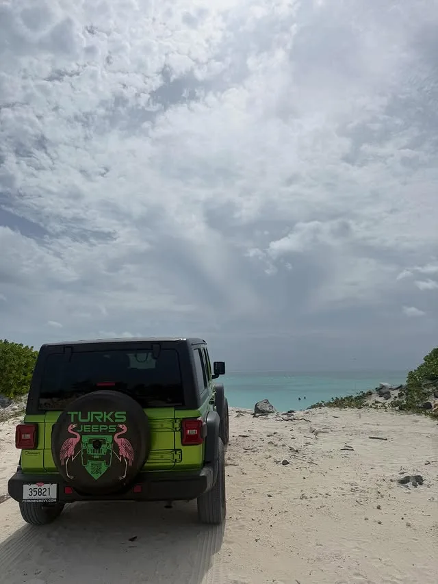 A lime green Turks Jeeps Wrangler on a sandy track above turquoise water