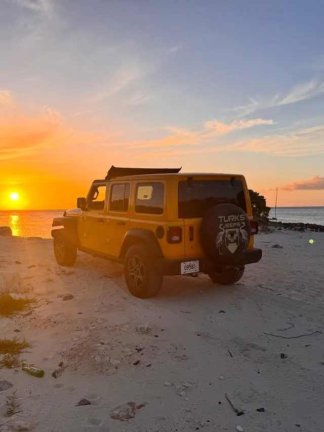 A yellow Turks Jeeps Wrangler by the water at sunset
